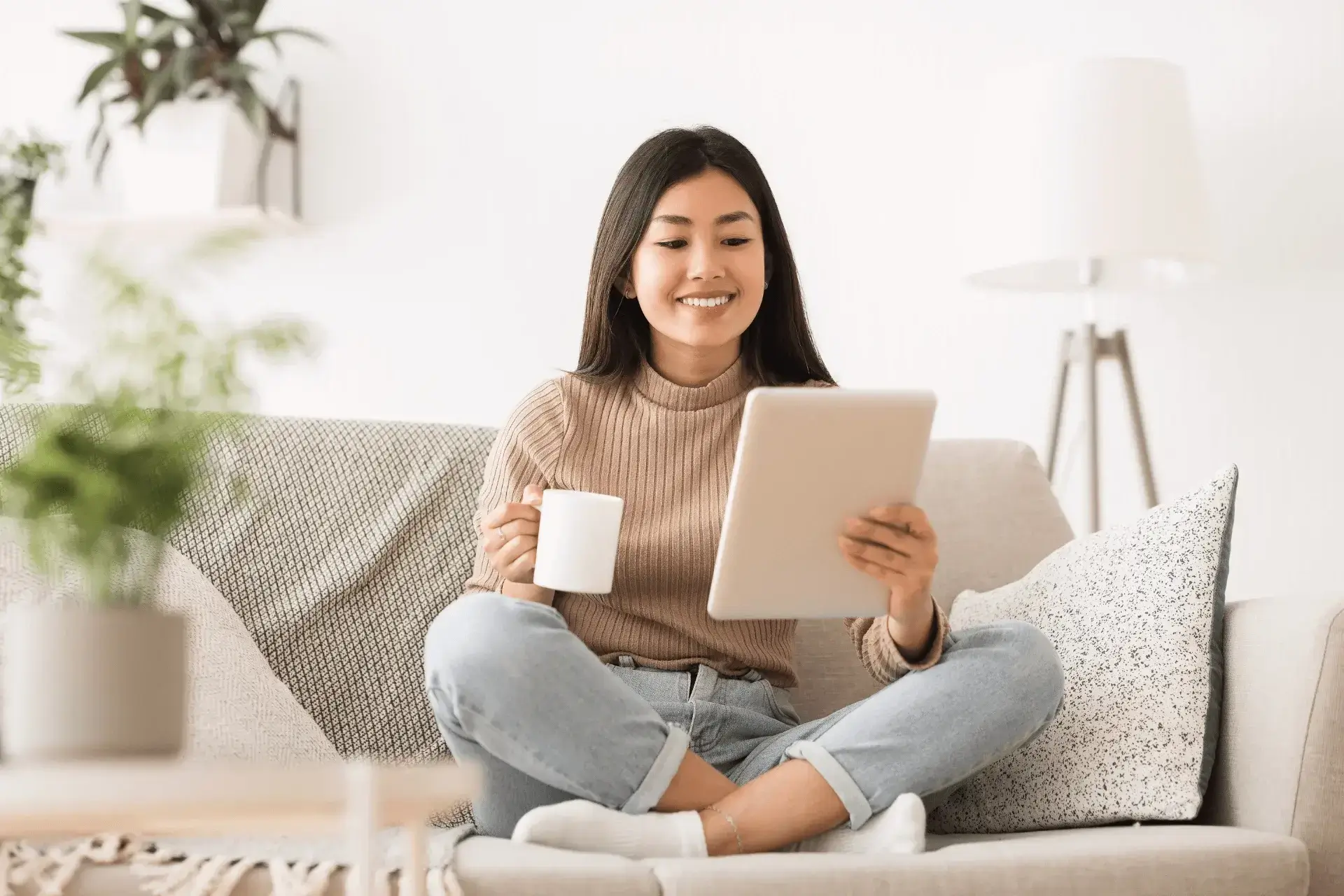 Mujer sentada en un sillón, leyendo en una tablet y sosteniendo una taza