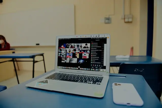 Laptop sobre un pupitre en un salón de clases, mostrando una videoconferencia