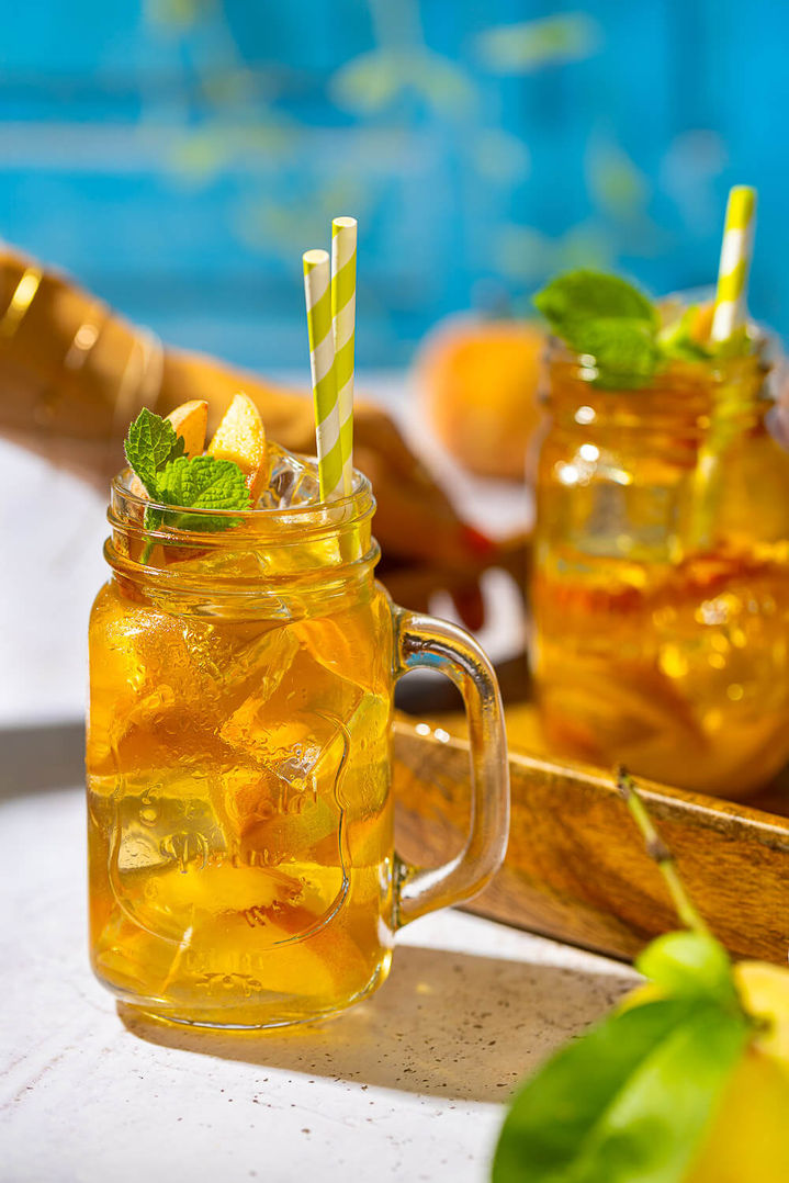 Selbstgemachter Eistee aus frischen Pfirsichen auf Holztablett und blauem mediterranem Hintergrund 