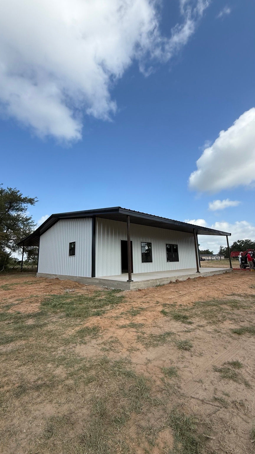 White metal barndominium with a wraparound porch