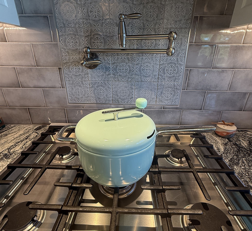 Photograph of a mint green Popsmith popcorn maker on a gas stove. Grey and black granite counter tops are on each side of the stove with a gray tile backsplash in the background. a Stainless steel pot filler is attached to the back wall. 