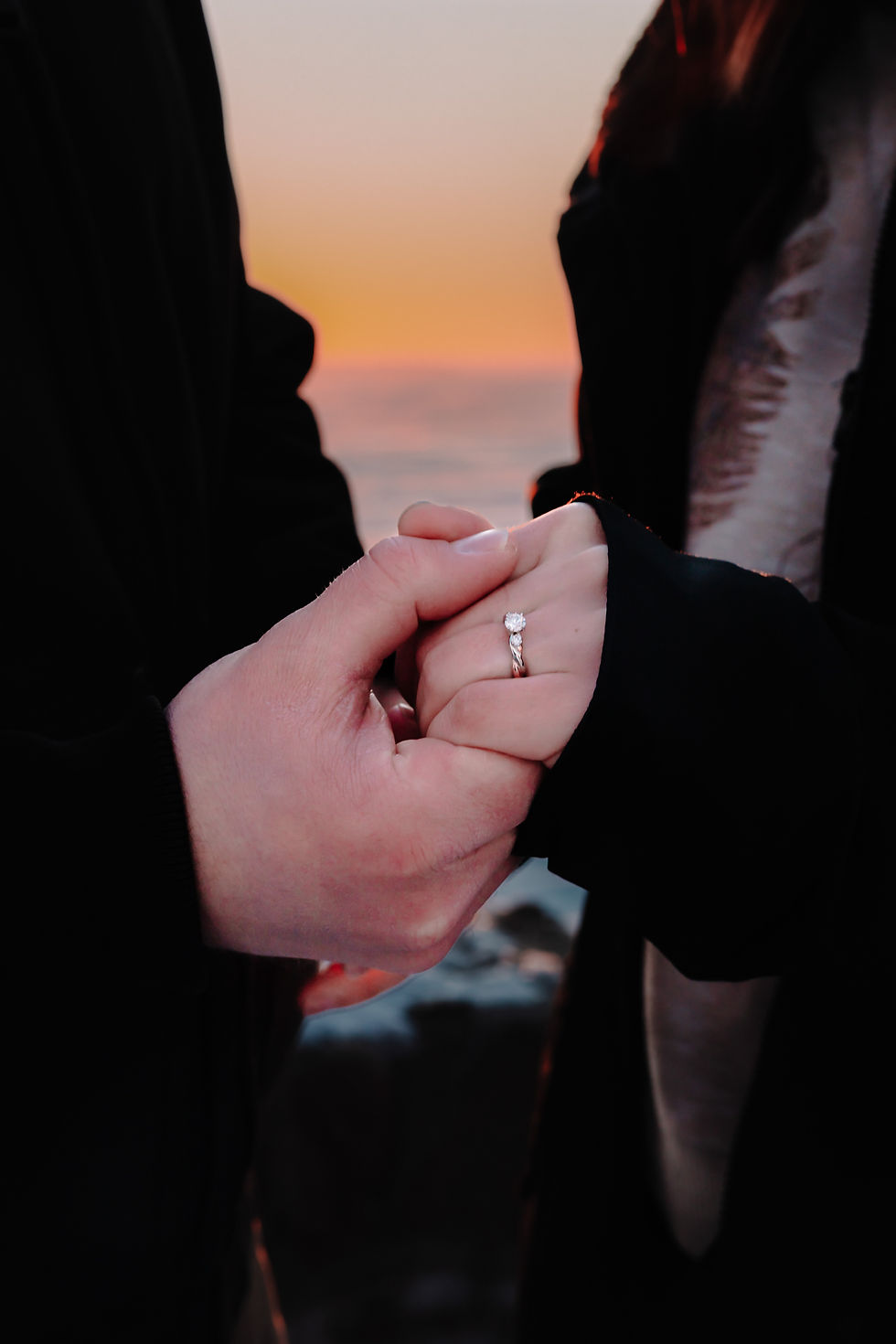 A couple in love hold on to hands after a surprise proposal with a beautiful diamond ring.