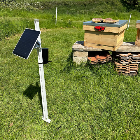 A beehive with the HAPSIE logo. Infront is a camera on a pole powered by solar panels.
