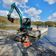 Floating barge carrying excavator across lake