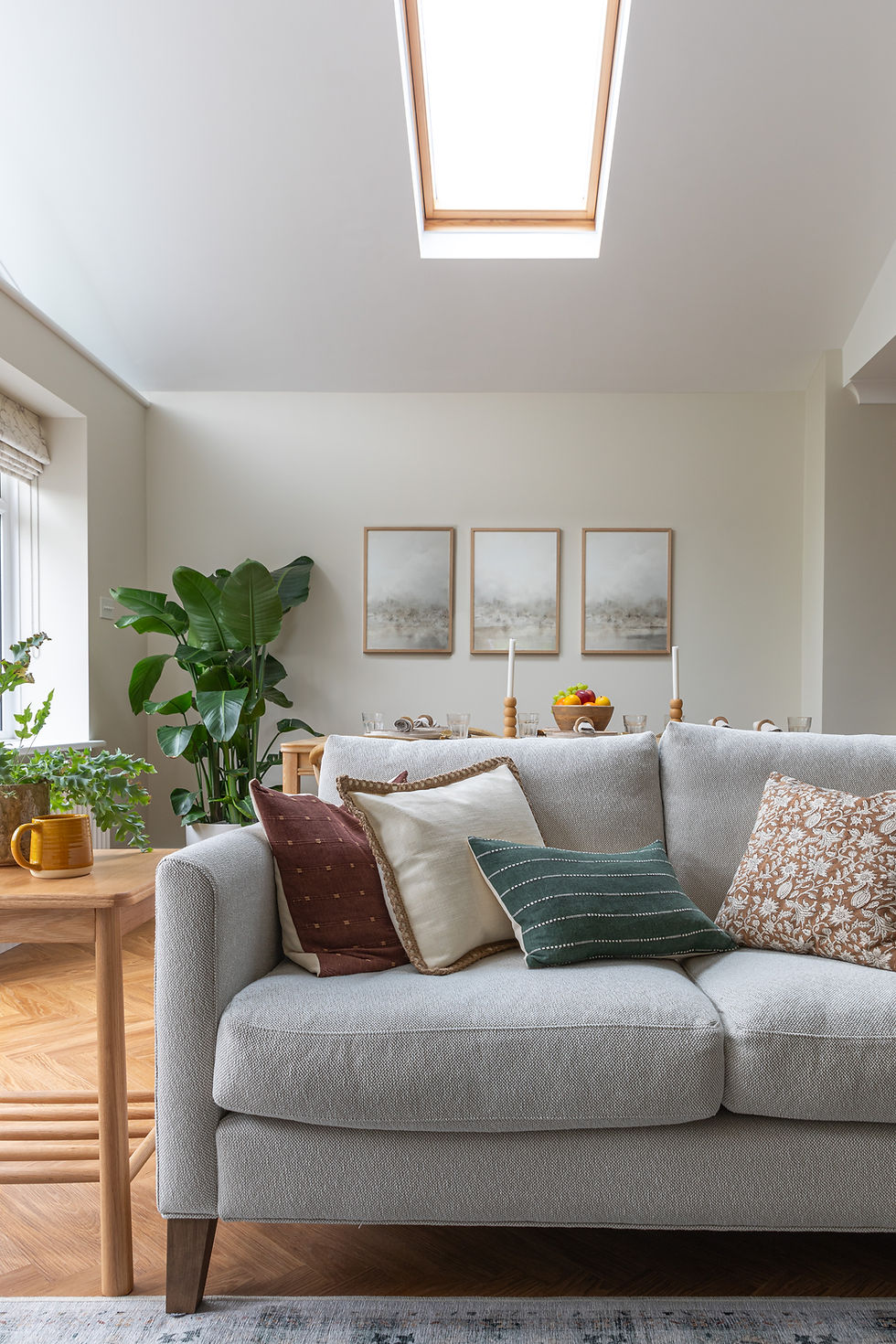 Bright dining room with a set table, wooden chairs, fruit bowl, and large window overlooking a garden. Blind at garden windows