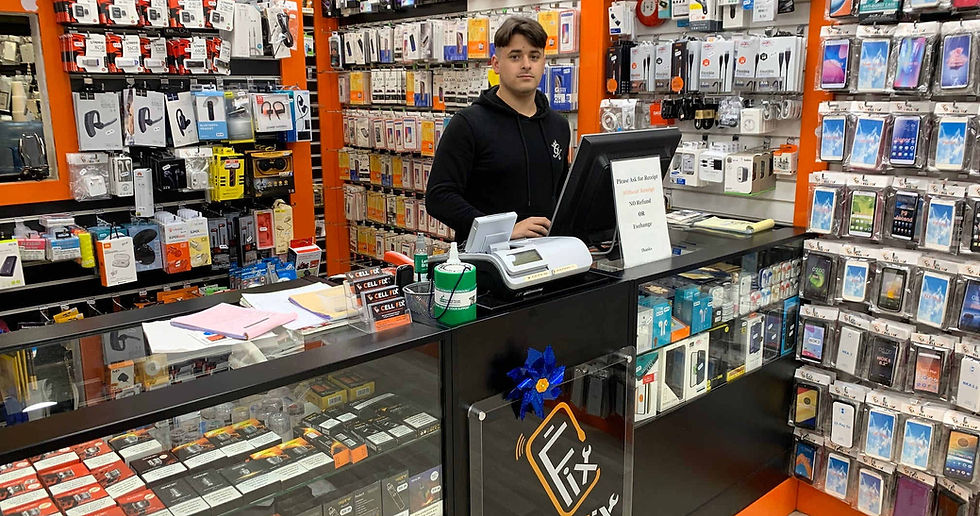 A store employee stands behind a counter in an electronics shop, surrounded by shelves filled with gadgets and accessories, conveying a busy retail atmosphere