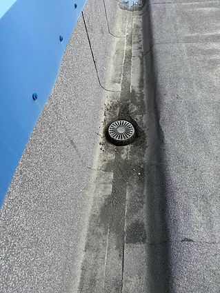 A rooftop drain surrounded by gravel and asphalt, with a hint of blue sky on the edge