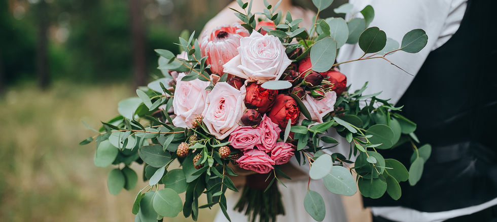 Bridal bouquet with pink roses, protea, and eucalyptus foliage in a loose, natural design held by the couple.