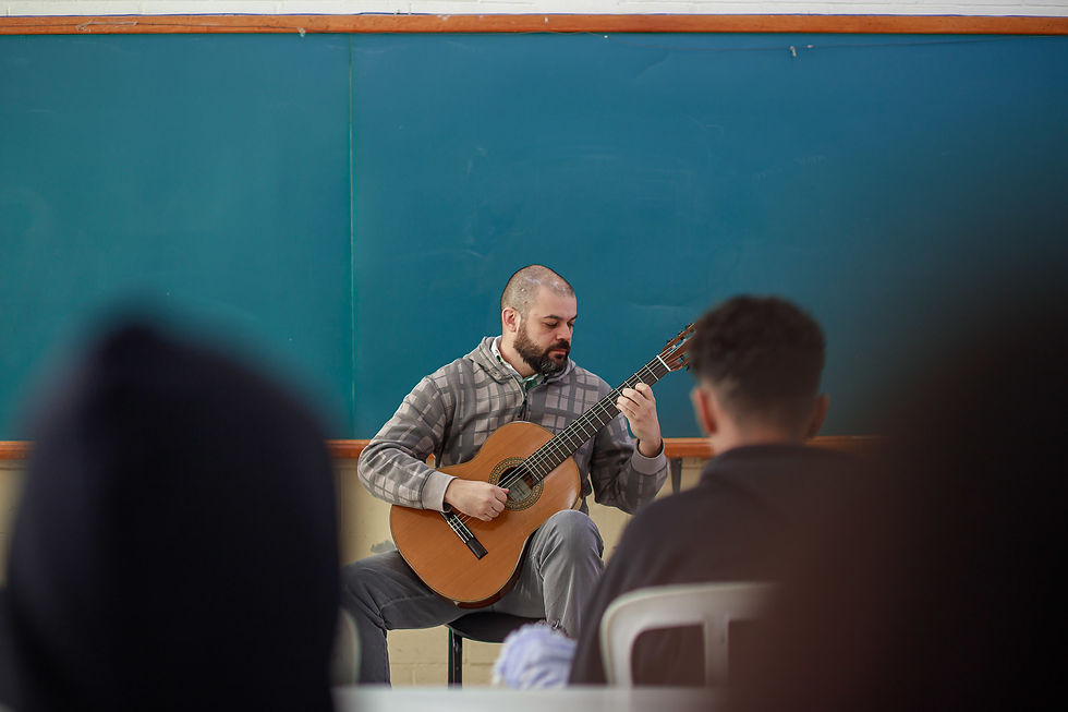 Homem tocando violão em frente a um quadro negro na Galeria.