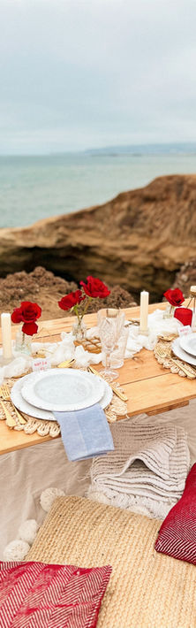 Romantic picnic on a cliffside overlooking the ocean. The table is decorated with giant red roses