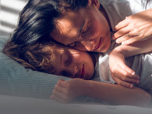 Mother and child sleeping peacefully, cuddled together under a blanket. Sunlight and shadows create a calm, serene atmosphere.