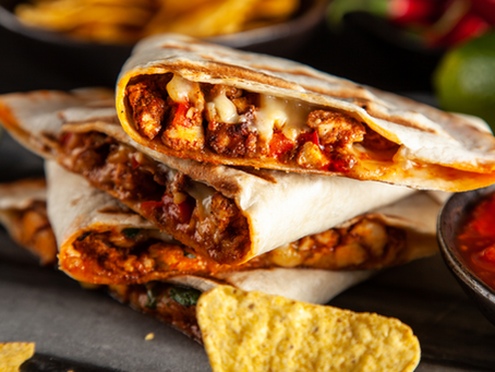 Stack of cheesy, grilled quesadillas with meat and barbeque sauce, surrounded by tortilla chips and a salsa bowl. Warm, appetizing setting.