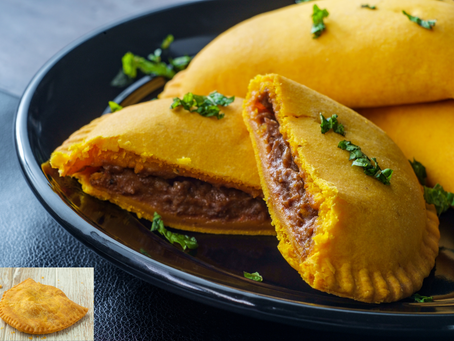 Yellow Curried Jamaican Beef Patties on a black plate, one cut open to show a brown filling. Garnished with chopped green herbs, evoking a savory mood.