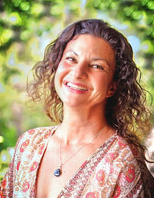Woman with brown curly hair smiling with green sparkling trees