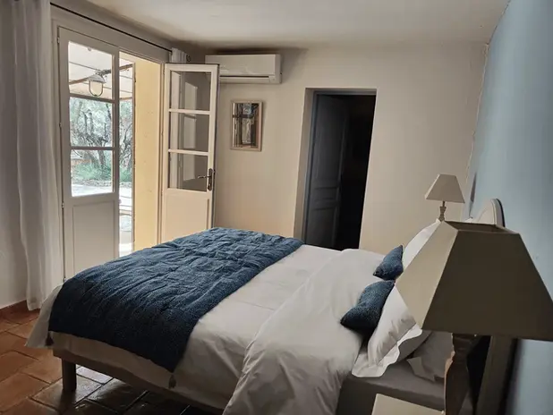 Chambre avec lit double, porte ouverte, rideaux blancs, murs clairs, vue sur jardin.