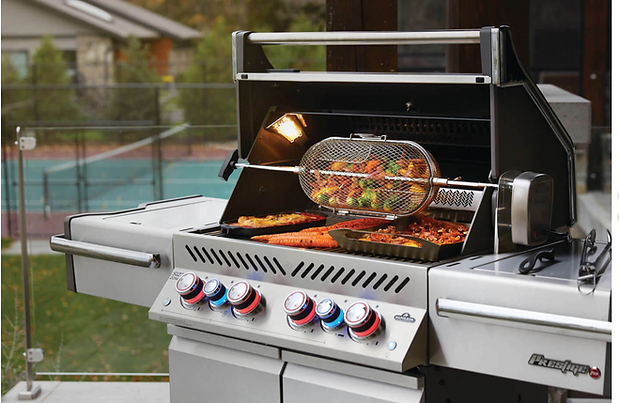 Napoleon built-in gas grill with rotisserie basket cooking chicken and vegetables, integrated into an outdoor kitchen setup.