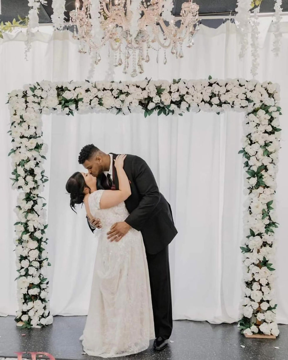 Bride and groom kissing under a white floral arch our most popular arch rental!