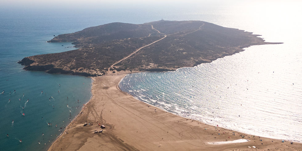 Prasonisi island from birdeye view, flat and wave side broken up by the sandy beach, lighthouse in the distance, many kiters and windsurfers in the water 