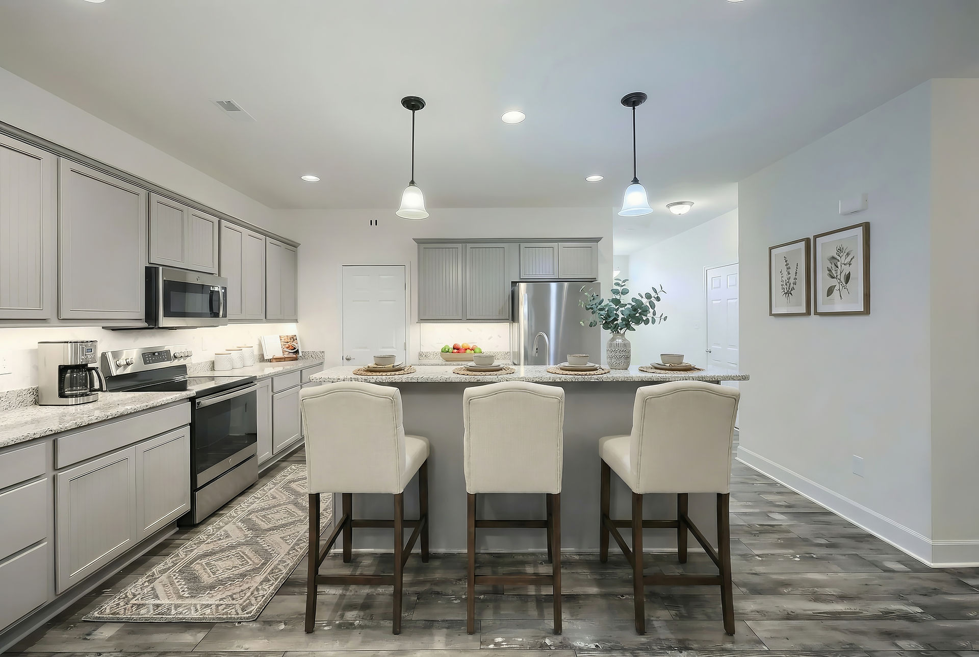 Virtually staged kitchen with gray cabinetry, granite counters, upholstered bar stools, decorative runner, and simple styling that highlights the open layout and island seating.