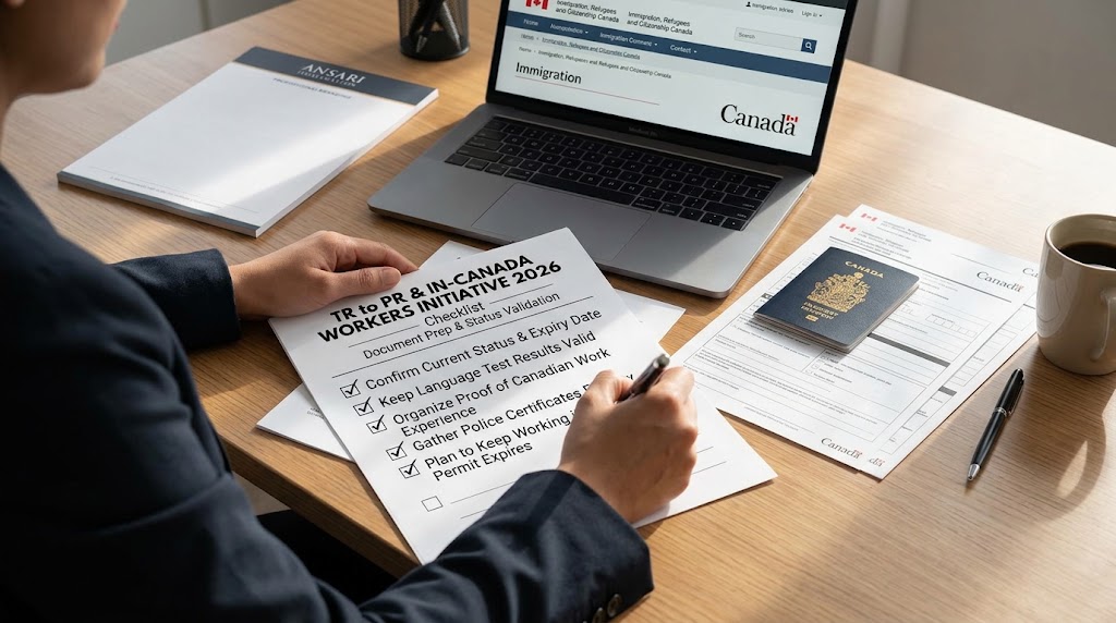Over-the-shoulder shot of an immigration consultant at a wooden desk filling out a checklist titled "TR to PR & IN-CANADA WORKERS INITIATIVE 2026 Checklist: Document Prep & Status Validation." Checked items on the list include: "Confirm Current Status & Expiry Date", "Keep Language Test Results Valid", "Organize Proof of Canadian Work Experience", "Gather Police Certificates Early", and "Plan to Keep Working if Permit Expires." On the desk is an open laptop showing the official Canadian immigration website (IRCC), a Canadian passport, additional official paperwork, a pen, and an "ANSARI IMMIGRATION" notepad.