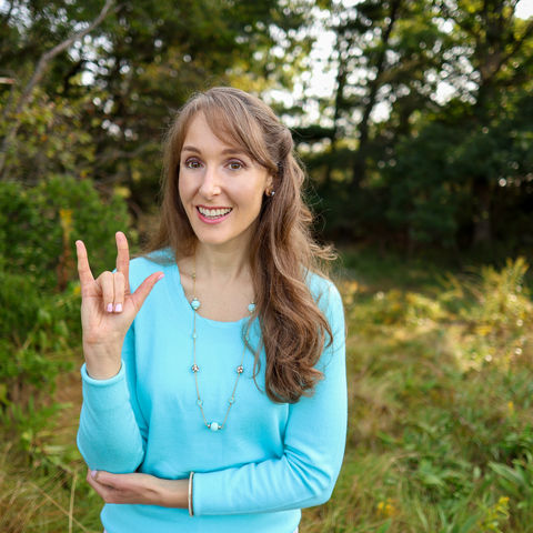 Bethany standing outside in a field signing the ILY sign in American Sign Language
