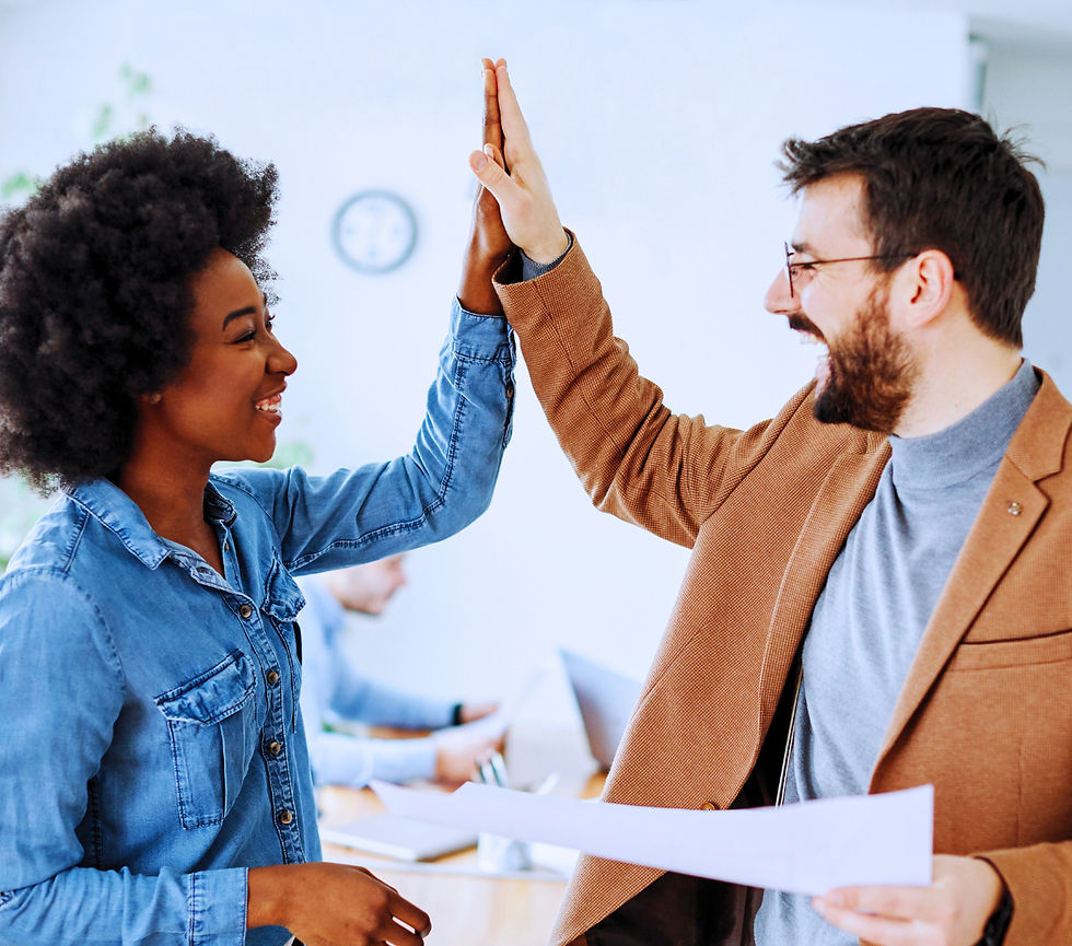 Professional black woman in a blue shirt and white man in a gray turtle neck shirt high fiving to celebrate an innovation win or success.