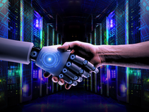 Human hand and robotic hand shaking in a glowing, futuristic server room. Blue digital patterns add a high-tech feel.