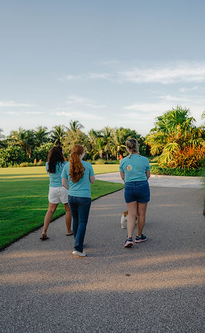 Three team members of Heidi and Hope walking away from the camera with palm trees in the background.
