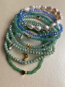Shades of green and blue crystal and gemstone bracelets with heart and moon charms. 