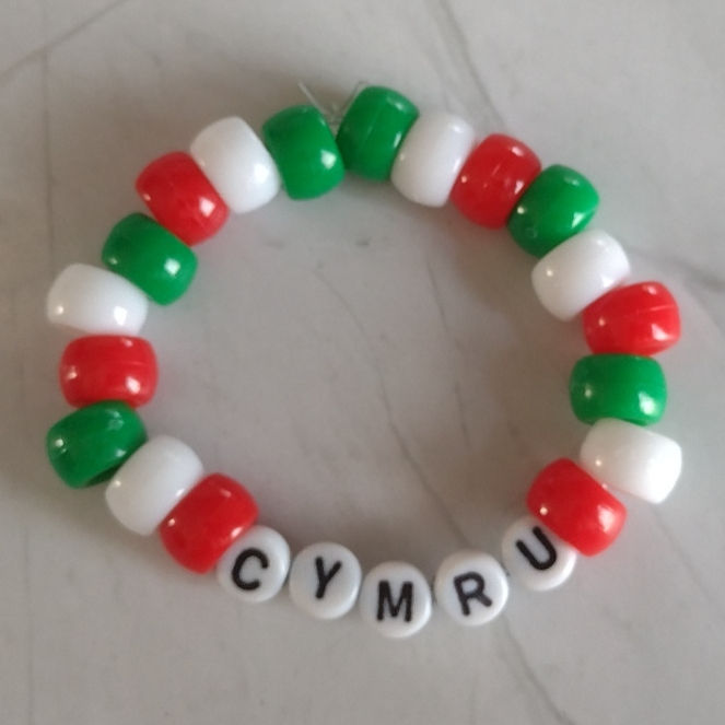a red, white and green beaded bracelet with the word Cymru (Wales) on it