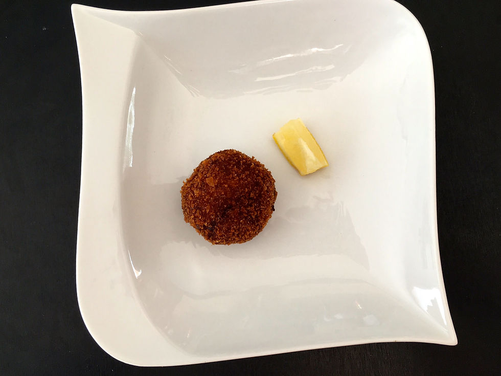 croquette de crevette et quartier de citron sur assiette blanche carrée, fond noir. Présentation élégante et minimaliste.