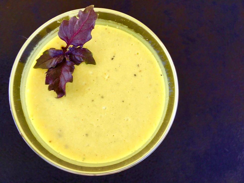 Bol de mousse jaune garni d'une feuille de basilic pourpre. Fond noir, texture crémeuse et ambiance apaisante.