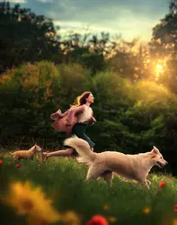 Ragazza che corre insieme ai suoi due cani giù per la collina piena di fiori durante un caldissimo tramonto primaverile.