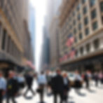 A bright sunny day in Wall Street, New York with professionals bustling the road and havin