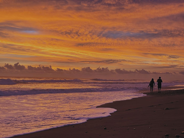 Couple strolling along the beach at sunset with vibrant orange and purple colors