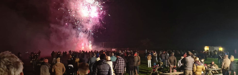 Wide landscape photo of a nighttime bonfire and fireworks crowd scene