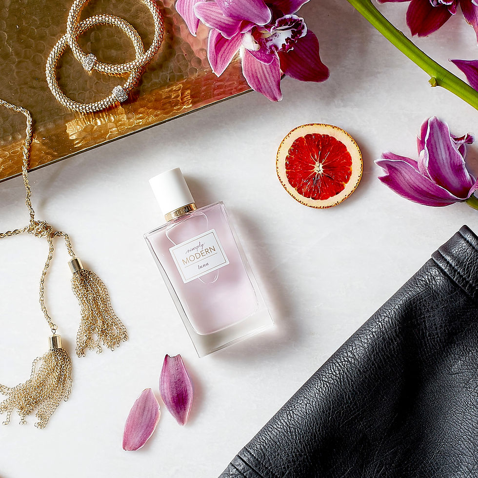 Perfume bottle with lilac liquid, surrounded by parts of leather, pink flower petals, blood orange, and gold