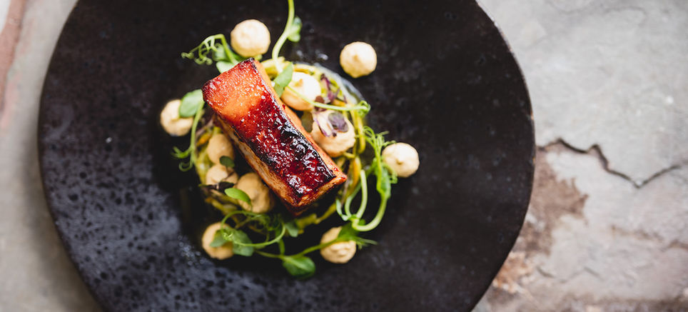 Gourmet dish with glazed fish, green sprouts, and white garnishes