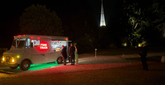 Lighted food truck serving customers at night, distant spire.