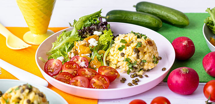 Plate of vegan salad with cherry tomatoes and grain salad, cucumbers and radishes on a colorful tabletop, bright fresh food display for children
