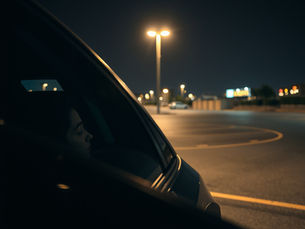 Sleeping child in a car at a dimly lit parking lot at night, with glowing streetlights and empty pavement.