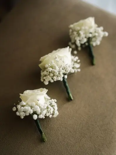 Three white rose and baby's breath boutonnieres for the groom or groomsmen.