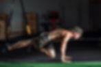 Man in camo shorts and cap doing TRX plank in a gym. Background includes exercise equipment. Bright lighting highlights muscles.