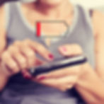Woman using a smartphone with a low battery icon overlay. She wears a gray top, and her nails are painted red. Focus on device and battery.