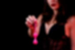 A woman in black lingerie holds a pink object with a string against a dark background. The mood is bold with contrasting colors.