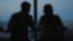 A silhouetted couple sits by a window, engaged in conversation, overlooking a cityscape at dusk. The mood is calm and intimate.