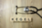 A stethoscope and wooden blocks spelling "KEGEL" on a woodgrain surface. The setting suggests a health or medical theme.