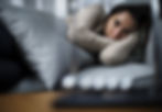 A woman lies curled up on a sofa, resting her head on a pillow with a distant, pained expression. Her eyes appear tired and tearful, capturing a moment of emotional vulnerability, sadness, or depression.