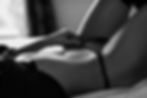 A close-up black and white image of a person lying down, adjusting black lingerie. Soft lighting creates a relaxed, intimate mood.