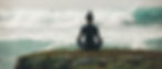 A person meditates in lotus position on a mossy rock by the ocean, with waves crashing in the background, creating a serene mood.